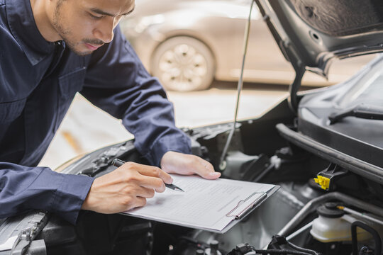 Auto check, car service shop concept. Automobile repairman writing job checklist on clipboard, mechanic checking engine to estimate repair machine, inspecting maintenance by engineer at vehicle garage