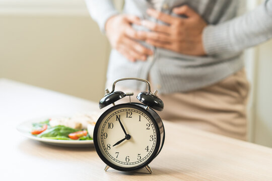 Intermittent fasting, diet healthy asian young woman dietary, having stomach ache, temptation hungry of brunch food in morning on table at home, waiting time to eat salad but not yet time first meal.