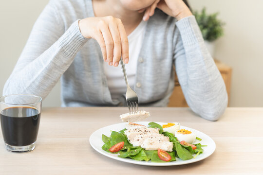 Diet bored concept, unhappy asian young woman, girl on dieting, holding fork at chicken breast on salad plate, dislike or tired with eat fresh vegetables. Nutrition of clean, healthy food good taste.
