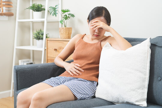 Flatulence asian young woman intolerance hand in stomach ache, suffer from food poisoning, abdominal pain and colon problem, gastritis or diarrhoea when at home. Patient belly, abdomen or inflammation