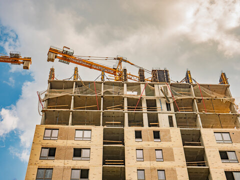 Modern residential apartment building under construction with a yellow tower crane against a dramatic sky
