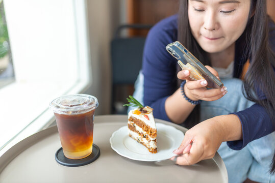 Woman taking photo of slice of cake with smartphone in cafe