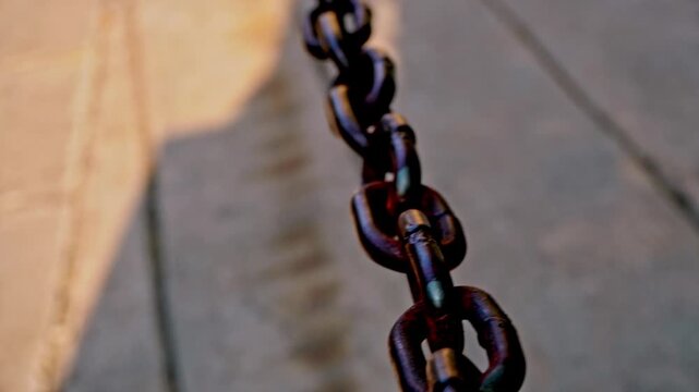 Dynamic motion shot of a swaying metal chain barrier outdoors on a sunny day in the historic old town district of Gresik, East Java, Indonesia.