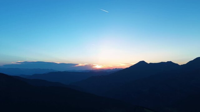 Layered mountain ridgelines silhouetted against a warm glowing horizon at Port de Cabus, Andorra, with aircraft contrails crossing the deep blue twilight sky above the Pyrenees