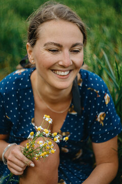 Woman Smiles While Picking Flowers in a Grassy Field