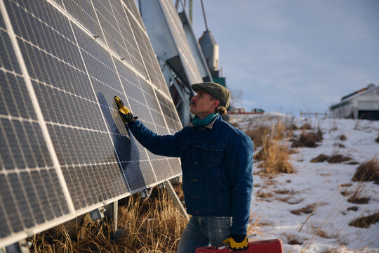 Worker Inspects Solar Panels at Snowy Field in Winter Afternoon