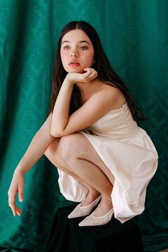Brunette model posing in white dress on green backdrop
