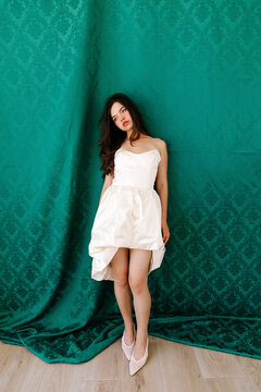 Caucasian woman posing in white strapless dress against green backdrop