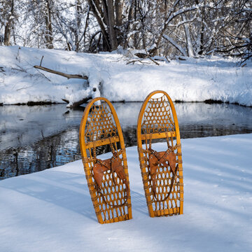 classic wooden snowshoes (Bear Paw) on a stream shore, winter scenery in Colorado