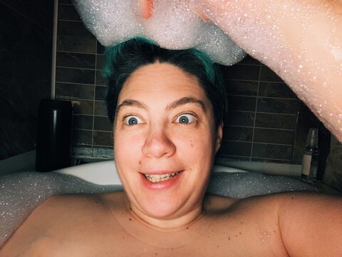 Person Smiles in Bathtub Full of Bubbles in Evening Light