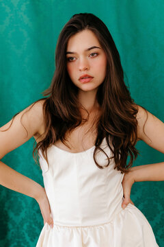 Young woman posing in elegant white dress on teal background