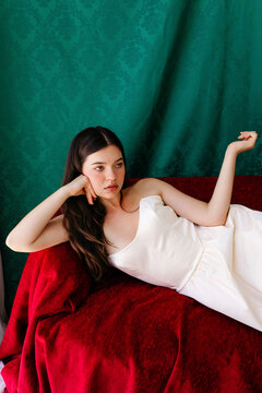 Woman reclining on red velvet sofa in white dress