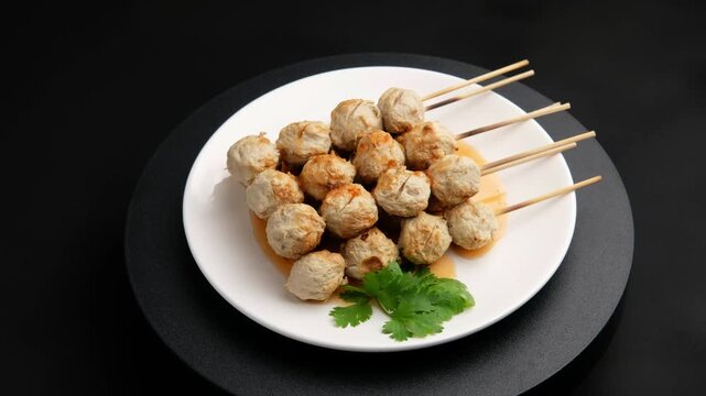 Charcoal grilled Thai Pork meatballs on skewers on white plate with chilli sauce.	