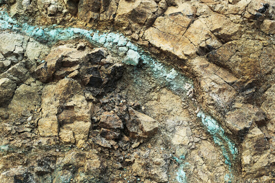 Blue-green mineral vein crossing weathered mountain rock