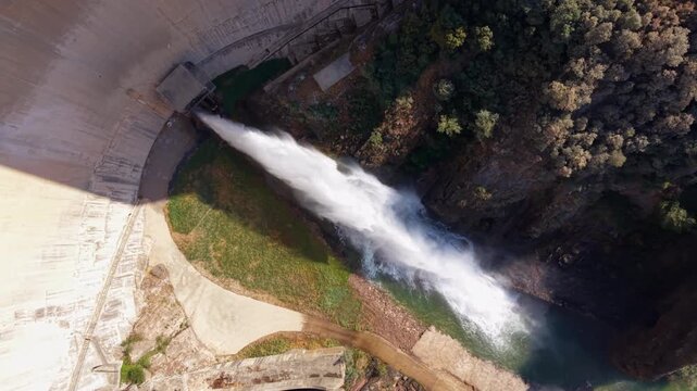 Overhead view of powerful water discharge from an outlet at Baells Dam in Catalonia, Spain, cascading into the river below with forested banks and rocky slopes