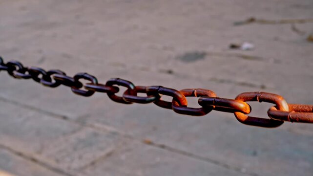Close up dynamic motion shot of a rusty metal chain fence swaying gently outdoors under warm sunlight in the historic old town of Gresik, Indonesia.