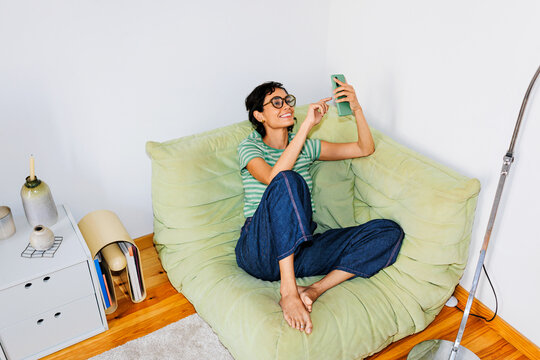 Woman relaxing on sofa using smartphone browsing content ugc