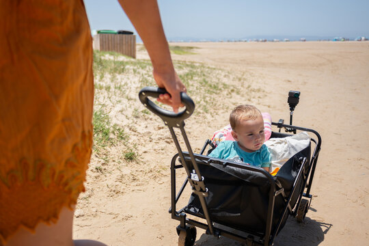 Parent pulling toddler in wagon at sandy beach