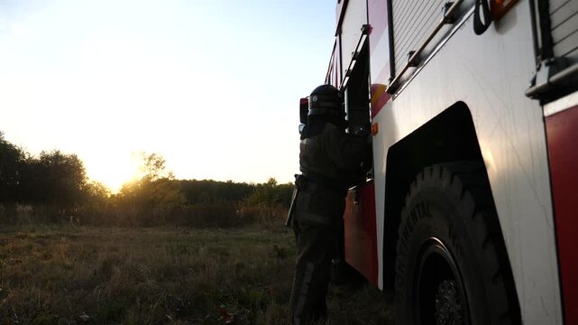 Young fireguard in uniform getting out equipment from the red truck. Professional fireman getting ready to extinguishes fire at countryside. Concept of environmental issues and global warming