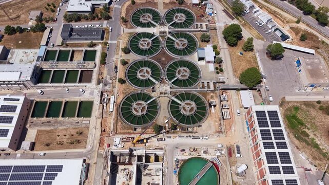 Overhead view of a drinking water treatment facility featuring symmetrical circular flocculation clarifiers with scraper arms, rectangular sand filtration basins, and rooftop solar panels