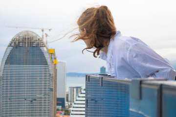 Fototapeta premium Smiling woman standing on high skyscraper balcony looking out over city skyline.