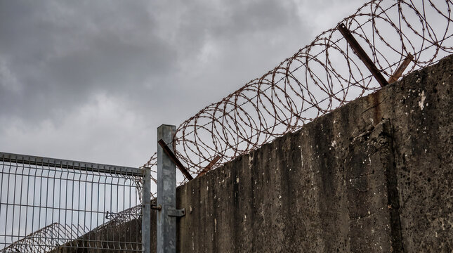 Security structure with barbed wire on top against a cloudy sky Generative AI
