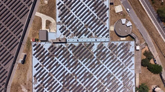Overhead view of a massive rooftop solar panel array on an industrial facility, with diagonally aligned rows split by maintenance walkways, showcasing large-scale renewable energy generation