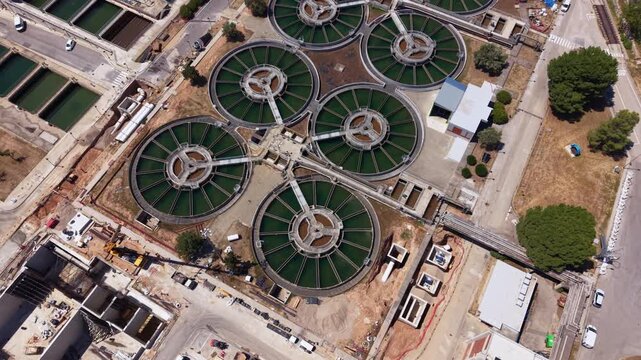 Overhead view of circular flocculation-decantation clarifiers connected by radial walkways at a drinking water treatment facility, surrounded by rectangular sedimentation basins