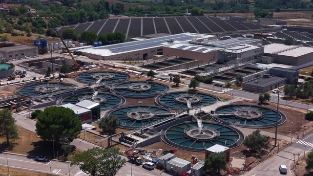 Aerial view of a water treatment facility featuring circular flocculation clarifiers, rectangular filtration basins, and main processing buildings with rooftop solar panels in a urban settings