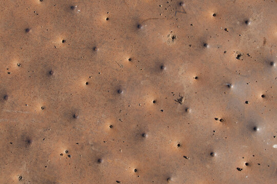 A close-up of a heavily corroded metal surface. The reddish-brown rust patina and uniform perforated pattern showcase the aesthetic decay of industrial materials.