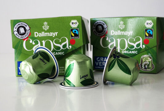 Green Dallmayr capsa organic coffee capsules standing in front of two green coffee boxes on a white reflective surface, featuring the brand name and leaf design.