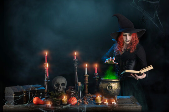 Witch casts spell, cauldron, boiling magic potion, candles. Woman learns witchcraft from a book, magician girl with red hair, dressed in Halloween attire and conical hat