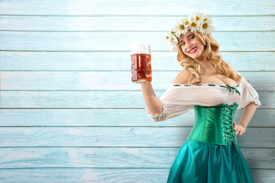 Midsummer woman waitress serving big beer mugs on wooden blue background. Blonde girl with wreath daisies flowers in her hair celebrating traditional beer festival in summer or spring
