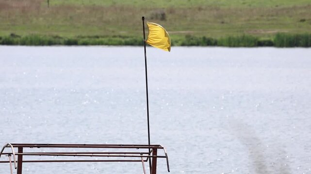Yellow warning flag fluttering on beach indicating potentially hazardous water conditions, slow motion