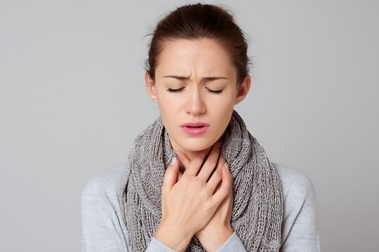 A young woman experiences a sore throat, wearing a scarf and looking uncomfortable with her eyes closed.