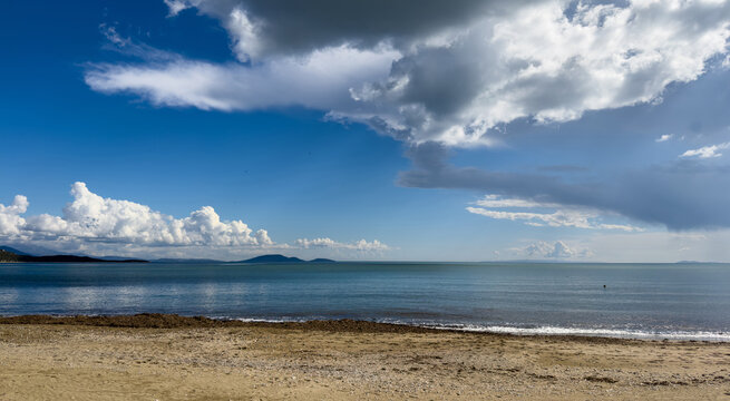 Towering winter clouds over calm blue sea and sandy shore in Schinias, Greece
