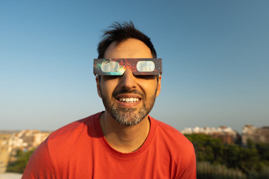 Man wearing protective solar eclipse glasses smiling outdoors