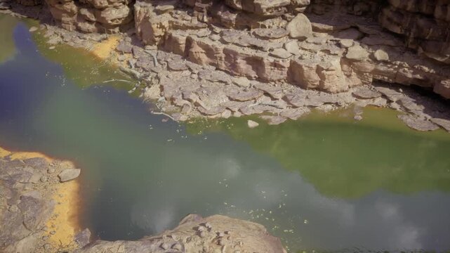 Aerial view of emerald canyon pool revealing sinuous shoreline and rocky terraces, topdown perspective shows algaetinted water, pebble patterns and textured