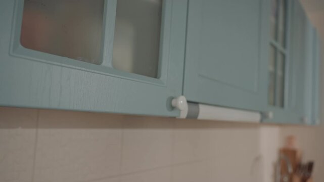 Soft morning hands open teal cabinet revealing frosted glass panel and underrail, slow deliberate motion, warm home interior, intimate domestic gesture by music lover, gentle fingertips on pastel