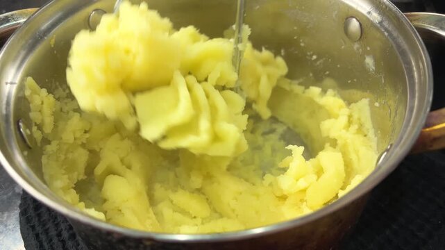 Potato masher crushing boiled potatoes into smooth puree in a bowl, homemade cooking, food preparation, comfort meal.