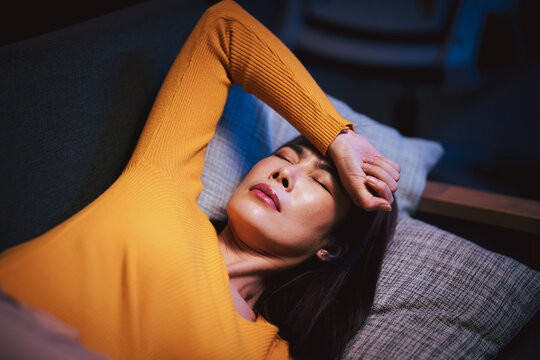 Adult Asian Woman Lying Down with Headache or Migraine Symptoms Relief on Sofa at Home. Seeking Treatment for Stress Sleepless and Pain
