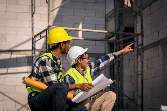 Asian Engineers Inspecting Construction Site Blueprint Plans Wearing Safety Helmets and Vests Examining Building Progress for Modern Architecture Design