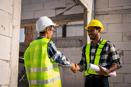 Two Adult Construction Workers Shaking Hands on Building Site Success Deal Young Asian Man Engineer Happy Smiling on Project Partnership Agreement