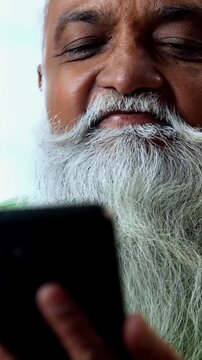 Indian mid age man watching smartphone reels while eating at home, stylish bearded male enjoying poha at breakfast table and streaming web series or comedy videos in modern kitchen lifestyle