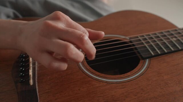 Closeup acoustic guitar picking hands caucasian. Soft fingerpicking on warm mahogany body, delicate touch and steady rhythm, focused songwriter practicing melody, intimate mood and gentle emotion