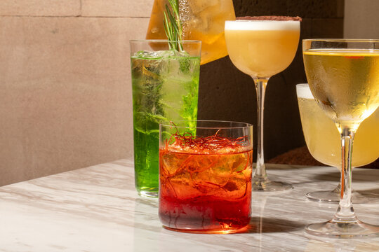 Three colorful craft cocktails on a marble bar with warm moody lighting, ideal for restaurant menus, cocktail blogs, nightlife editorials, social media and beverage marketing