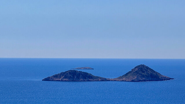 Twin rocky islands on a calm blue sea under clear soft daylight, minimalist travel seascape suitable for travel editorial, website header, social media, and background imagery