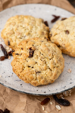 Baked cookies. Tasty food. Golden round treats served on rustic plate with scattered oat raisins ingredient on wrinkled wrapping paper.