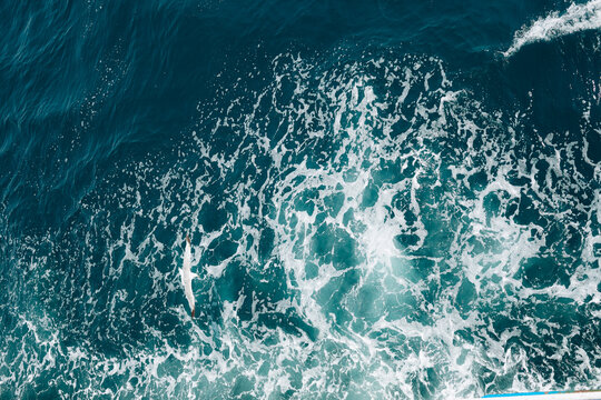 Abstract aerial texture of crystal blue ocean water with swirling waves and white sea foam.