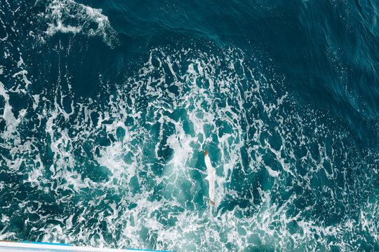 Turquoise ocean water with white foamy waves creating a natural abstract texture and vibrant blue background.
